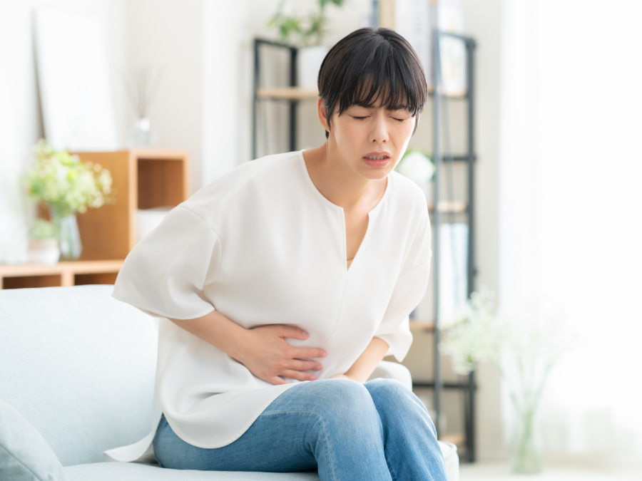 ソファに座ってお腹が痛そうな女性