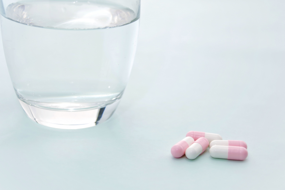 ピンク色のカプセル薬とコップに水が入った写真